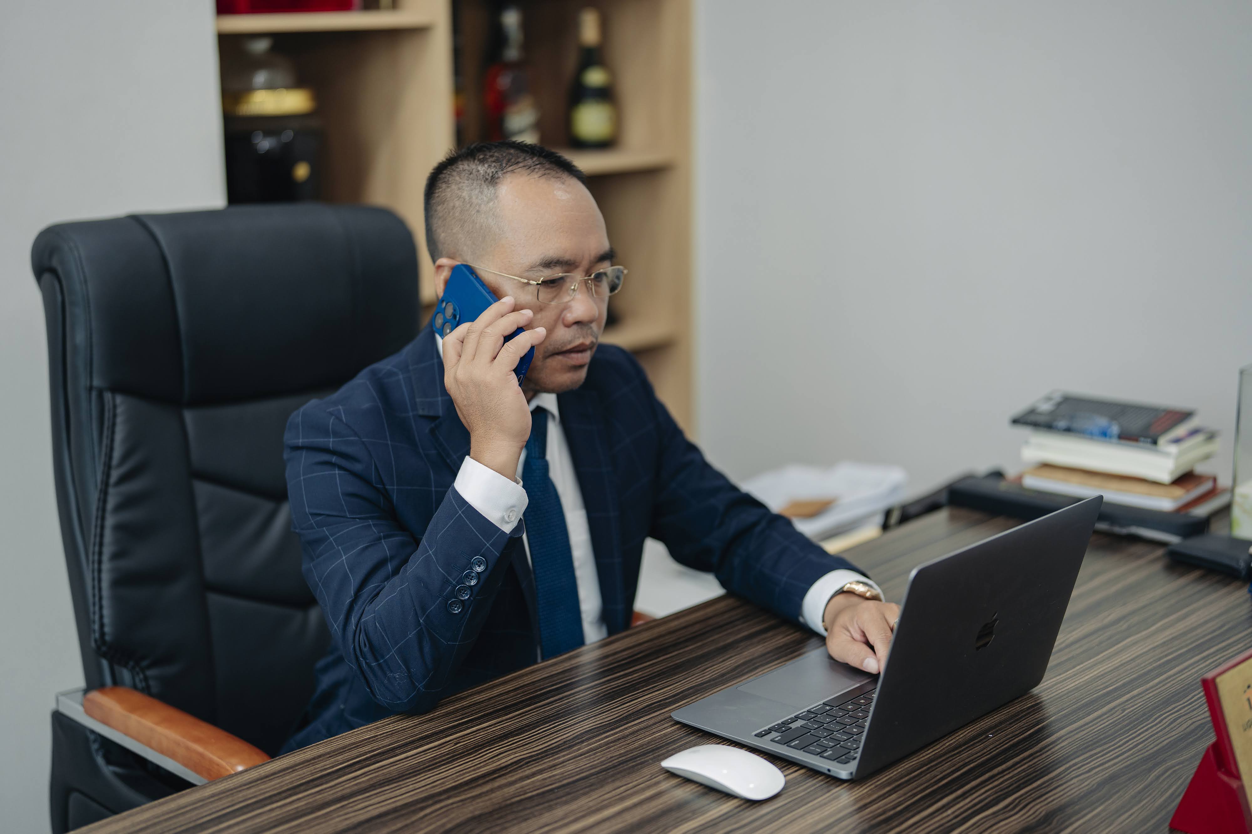 A person in a suit talking on a phone and using a computer